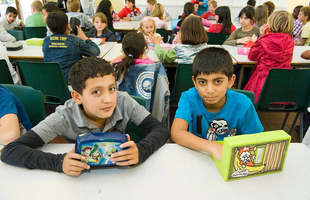 Leerlingen eten hun van thuis meegebrachte boterhammen in de refter van hun school