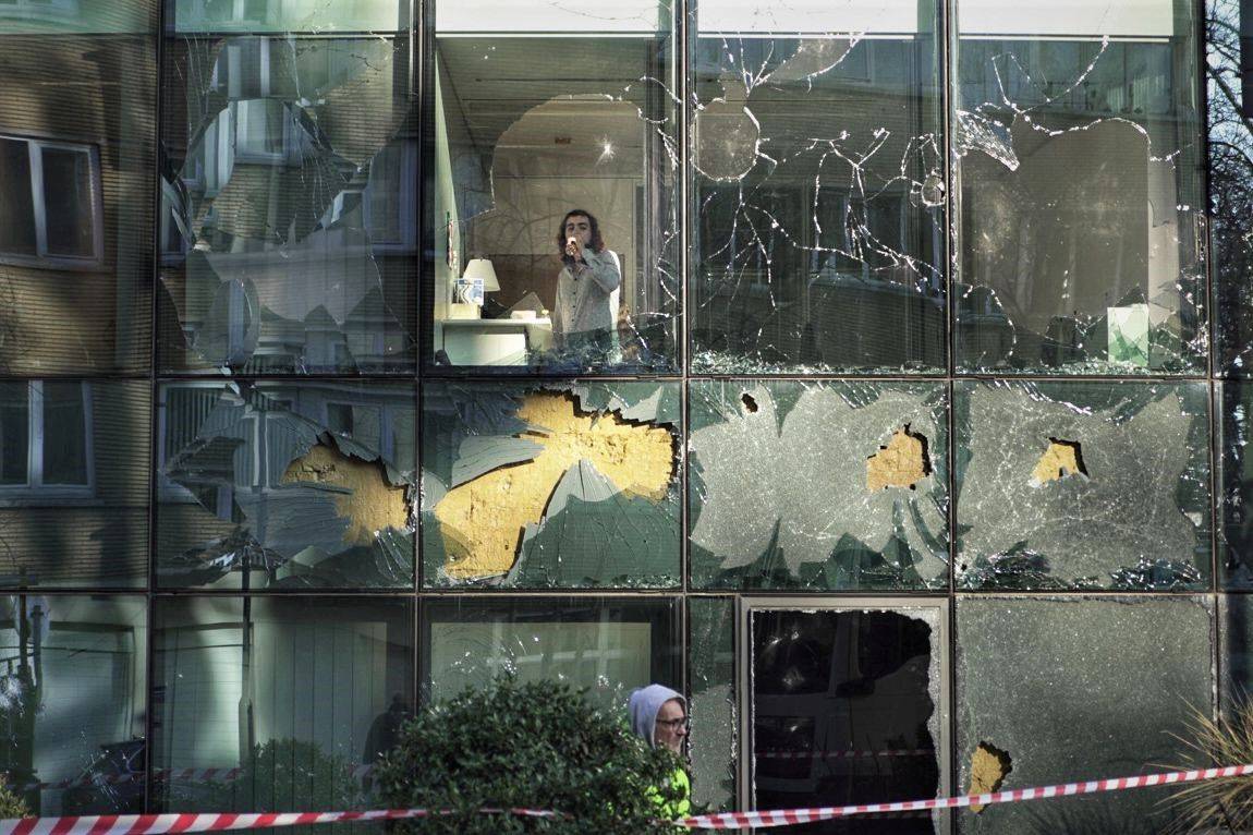 Een man drinkt iets, hij kijkt naar buiten door een raam dat beschadigd werd bij de coronabetoging van 23 januari 2022