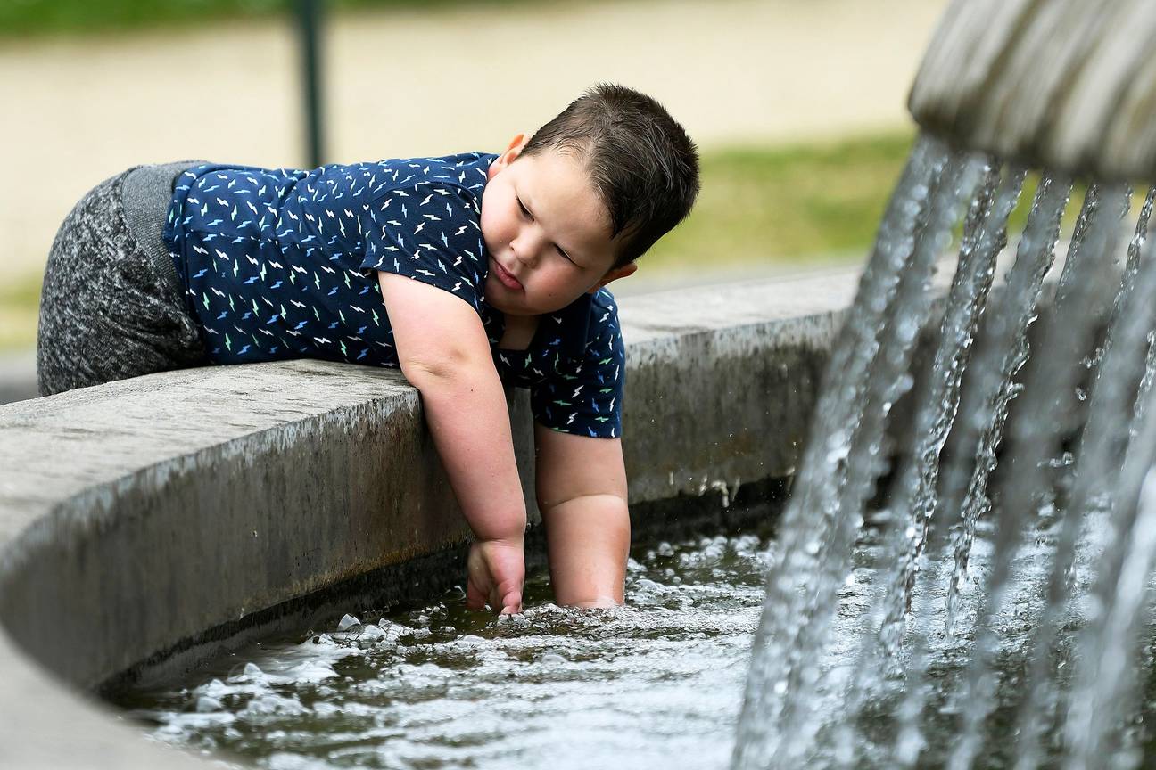 Een kind bij een fontein aan het atomium op een warme dag