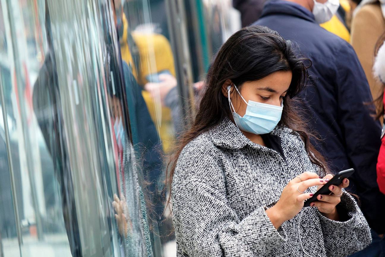 Een vrouw met mondmasker en een smartphone aan de Apple-flagshipstore aan de Guldenvlieslaan