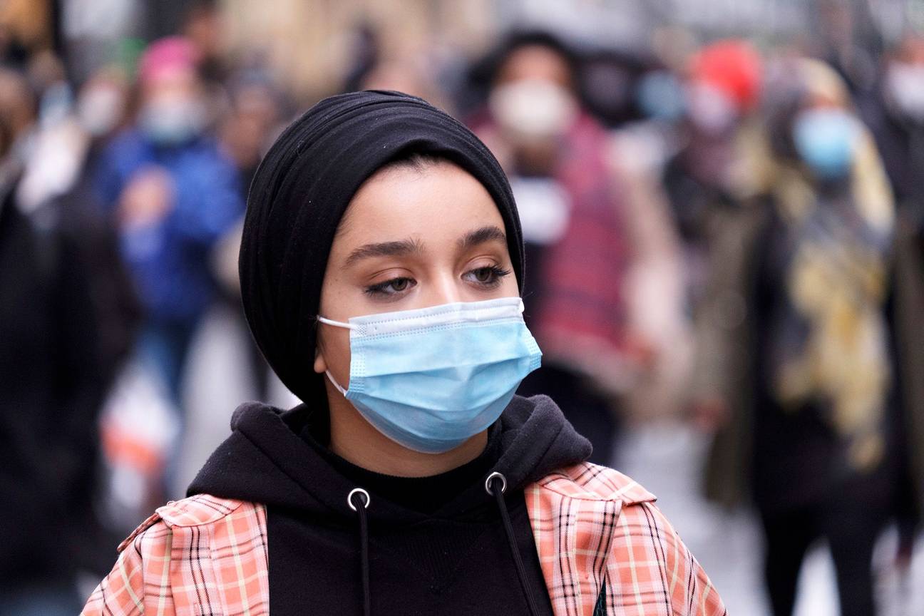 Een vrouw met mondmasker en hoofddoek in een winkelstraat