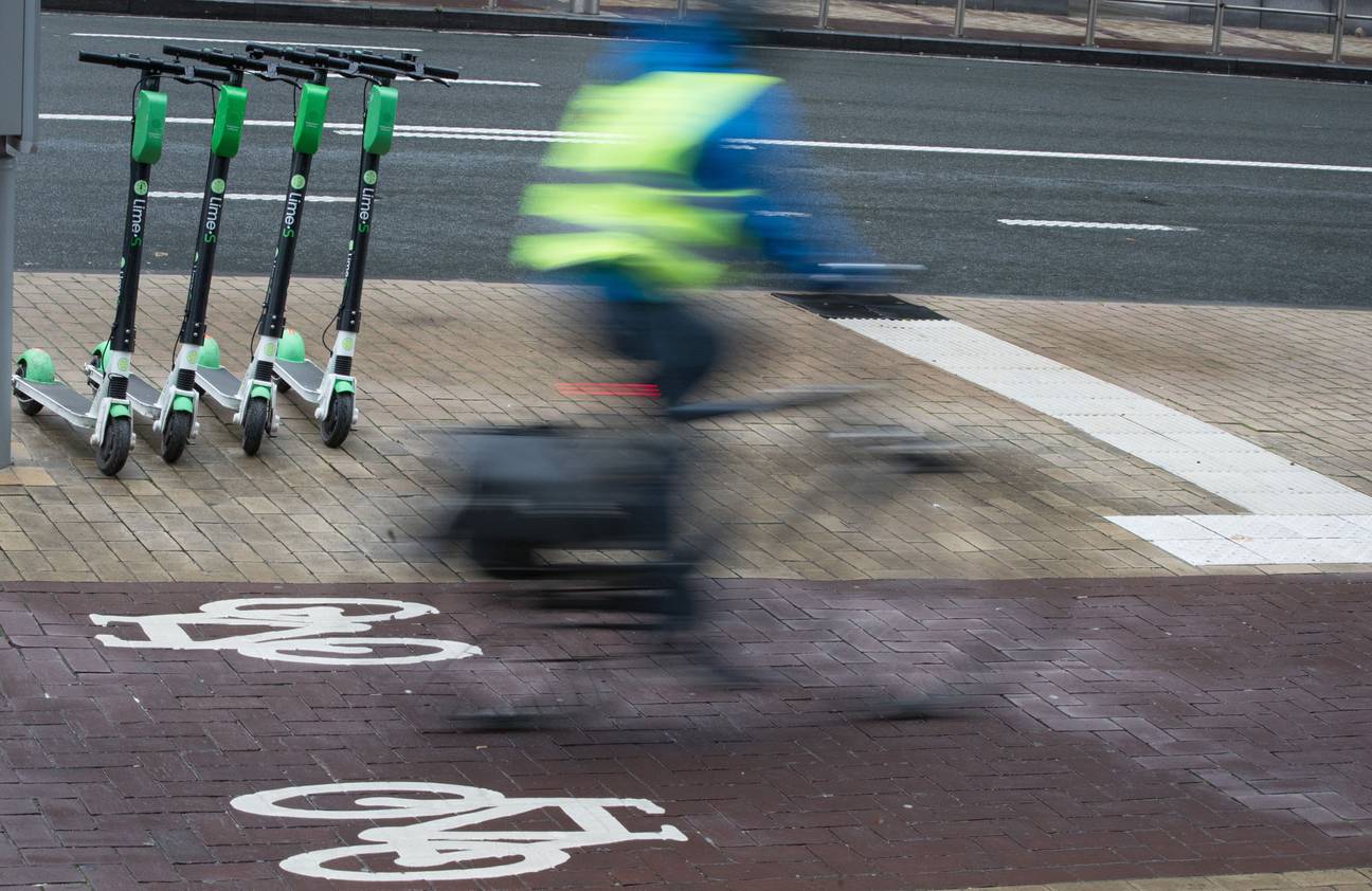 Een fietser rijdt langs geparkeerde deelsteps van Lime