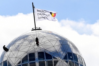 14 april 2020: op de bovenste bol van het atomium wordt een vlag gehesen om de zorgsector in België te bedanken voor hun werk om de coronacrisis te bedwingen: bedankt/merci
