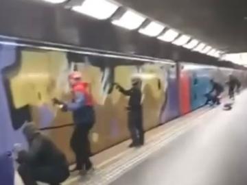 Verschillende mensen spuiten graffiti op een metrotrein die aan het perron in Weststation staat te wachten
