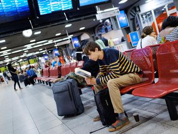 Lezend wachten op een trein in de centrale hal van het station Brussel-Zuid.