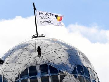 14 april 2020: op de bovenste bol van het atomium wordt een vlag gehesen om de zorgsector in België te bedanken voor hun werk om de coronacrisis te bedwingen: bedankt/merci