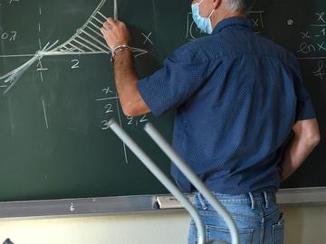 Leraar aan het schoolbord met een mondmasker op