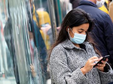 Een vrouw met mondmasker en een smartphone aan de Apple-flagshipstore aan de Guldenvlieslaan