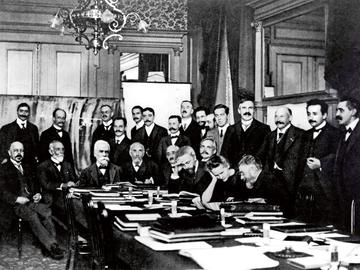 De eerste Solvayconferentie in Brussel, met Marie Curie aan tafel en Albert Einstein als tweede van rechts. Ernest Solvay is de derde van links, zittend, maar hij was niet aanwezig toen de foto werd genomen. Zijn portret werd er later ingeplakt.