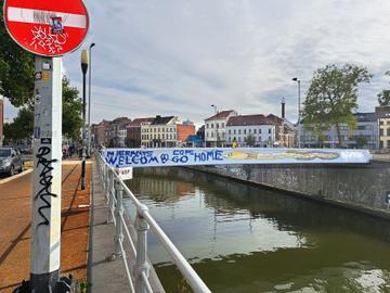 13 september 2022: een nieuw opschrijft op de passerelle over het kanaal ter hoogte van het MIMA:  "Migrants welcom(e), Cops go home"