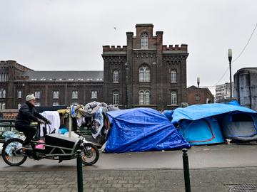 Januari 2023: asielzoekers in een geïmproviseerd tentenkamp aan de brug over het kanaal bij het Klein Kasteeltje, de verbiding tussen de Koolmijnenkaai en de Negende Linielaan aan de Kleine Ring. Een man op een cargobike fietst erlangs