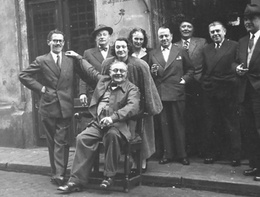 Op de foto zie je Geert van Bruaene op de stoel voor Het Goudblommeke in Papier en omringd door zijn vrienden. Van links naar rechts: Marcel Mariën, Camille Goemans, Irène Hamoir, Georgette Magritte, E.L.T. Mesens, Louis Scutenaire, Réné Magritte en Paul