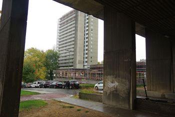 14 oktober 2022: het zo goed als volledig gerenoveerde woonblok 2 op de Modelwijk in Laken, gezien vanonder de steunpilaren van blok 1. De werf tussen de twee blokken toont waar de nieuwe bibliotheek moet komen, ter vervanging van de oude lager op de site